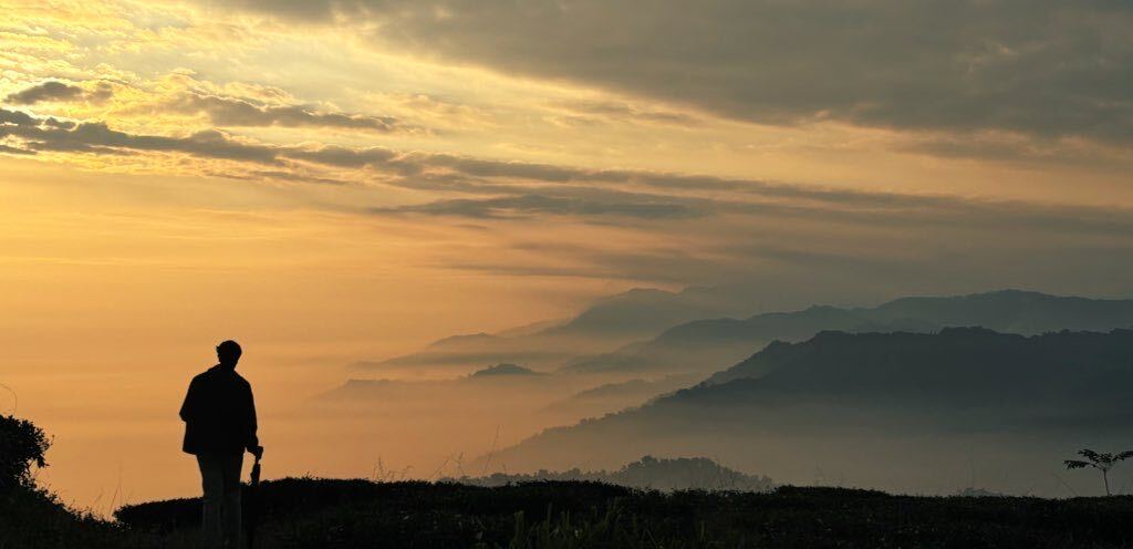 A silhouetted figure overlooking layers of misty hills beneath a golden sky
